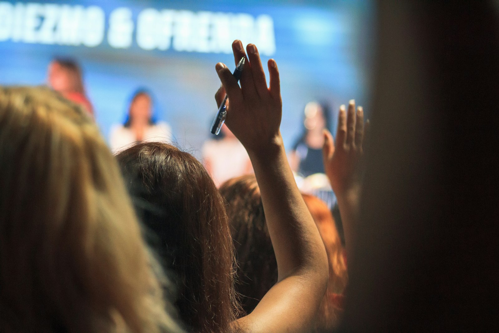 People in an audience raising their hands to ask questions at a conference